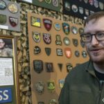 Стів Андре на тлі зібраної ним колекції нарукавних знаків під час відкриття виставки у Національний військово-історичний музей України. За його спиною розміщені стенди з десятками шевронів і патчів різних підрозділів Сил оборони України та суміжних структур. Колекція впорядкована за тематикою й оформлена у вигляді музейної експозиції, що дозволяє розглянути кожен знак окремо. Образ Стіва Андре на фоні експонатів підкреслює особисту причетність колекціонера до створення цієї унікальної виставки.