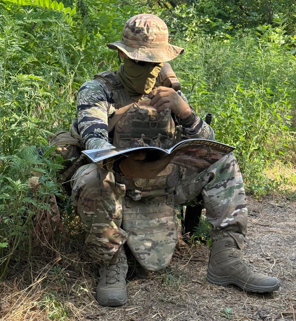 Український захисник у польових умовах під час короткого відпочинку за читанням журналу.