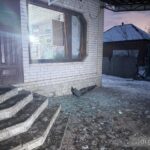 На зображенні зафіксовано будівлю з пошкодженим вікном та вибитим склом, уламки якого лежать на сходах і біля входу. Частина фасаду має сліди руйнувань. Подія зафіксована у темну пору доби.