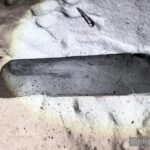 На снігу лежить металевий фрагмент прямокутної форми. Поверхня деталі має сліди кіптяви та деформації. Поруч помітні інші дрібні уламки.