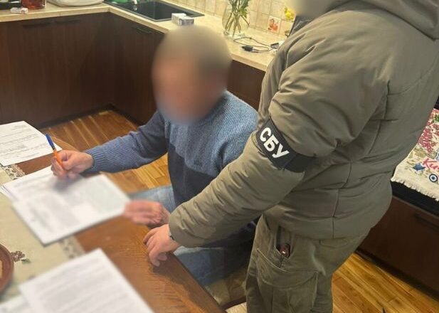 Чоловік сидить за столом. Поруч стоїть співробітник СБУ