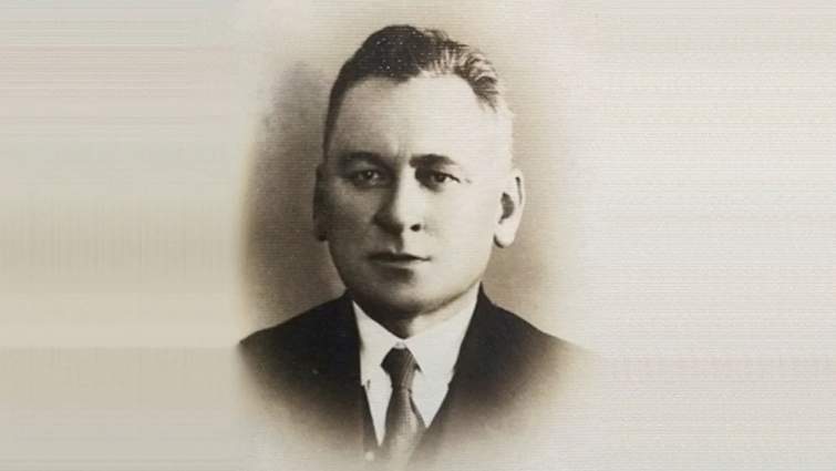 Чорно-білий студійний портрет чоловіка в костюмі й краватці зосереджує увагу на його строгому, зібраному погляді. Світлий нейтральний фон підсилює відчуття офіційності та стриманості образу.