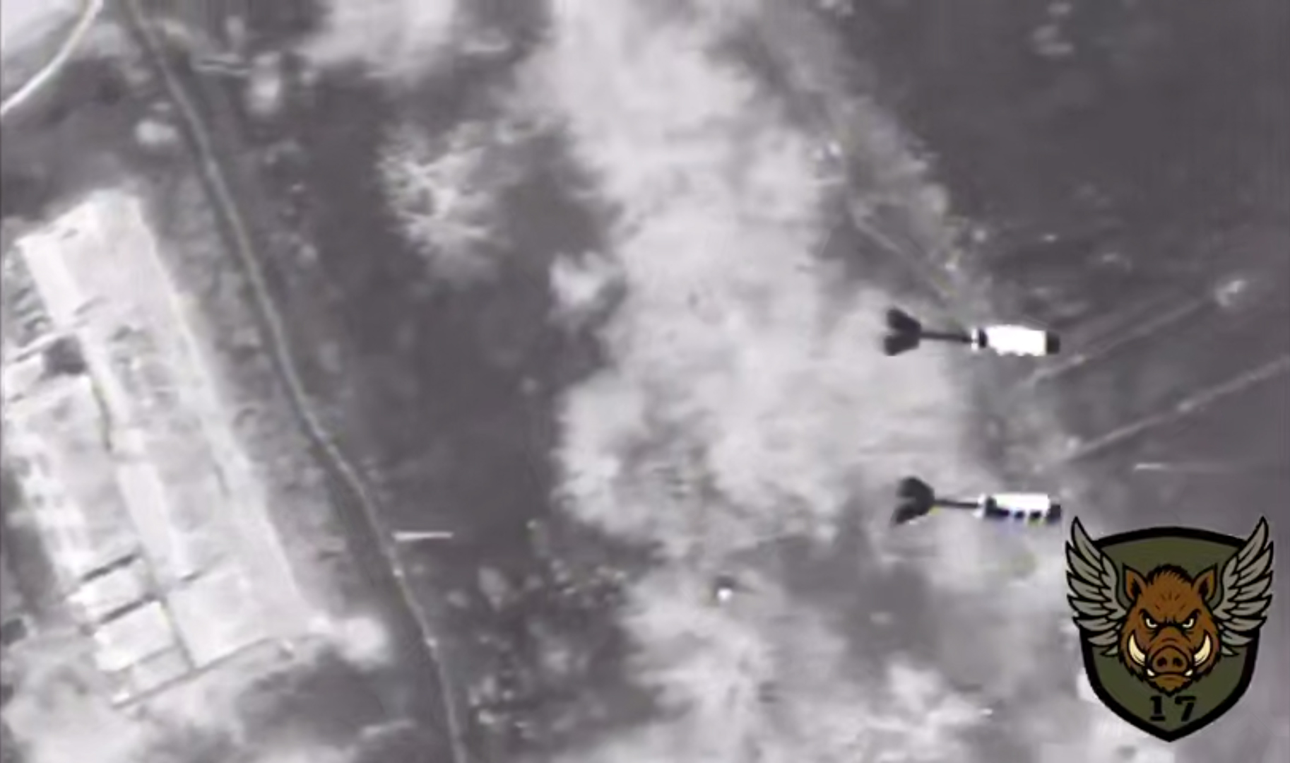 Чорно-білий аерознімок фіксує момент падіння двох авіаційних боєприпасів над місцевістю з дорогами та будівлями. У правому нижньому куті видно емблему з крилатим кабаном і числом 17.
