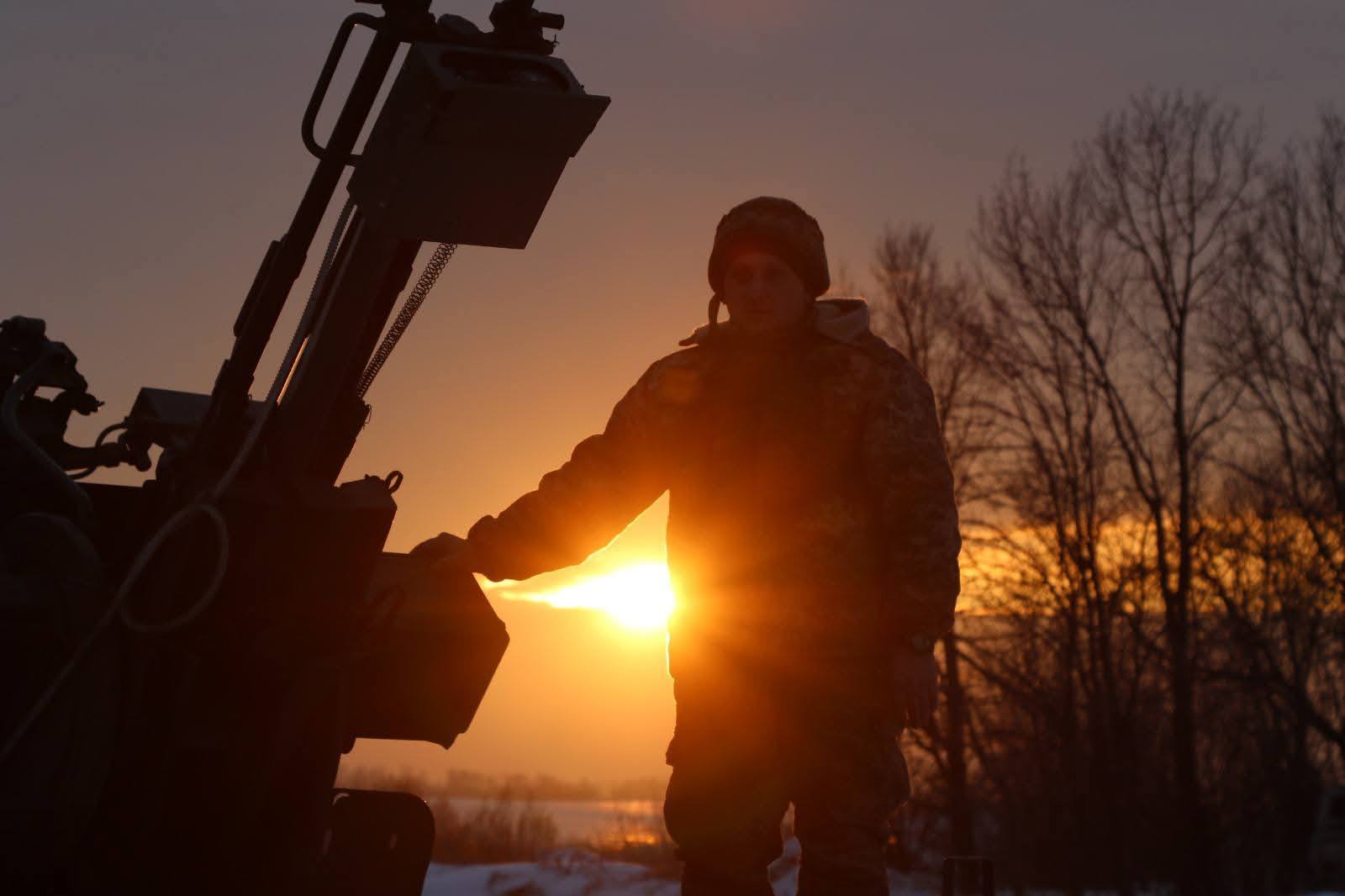 Чоловік біля артсистеми на тлі сонця, що сідає