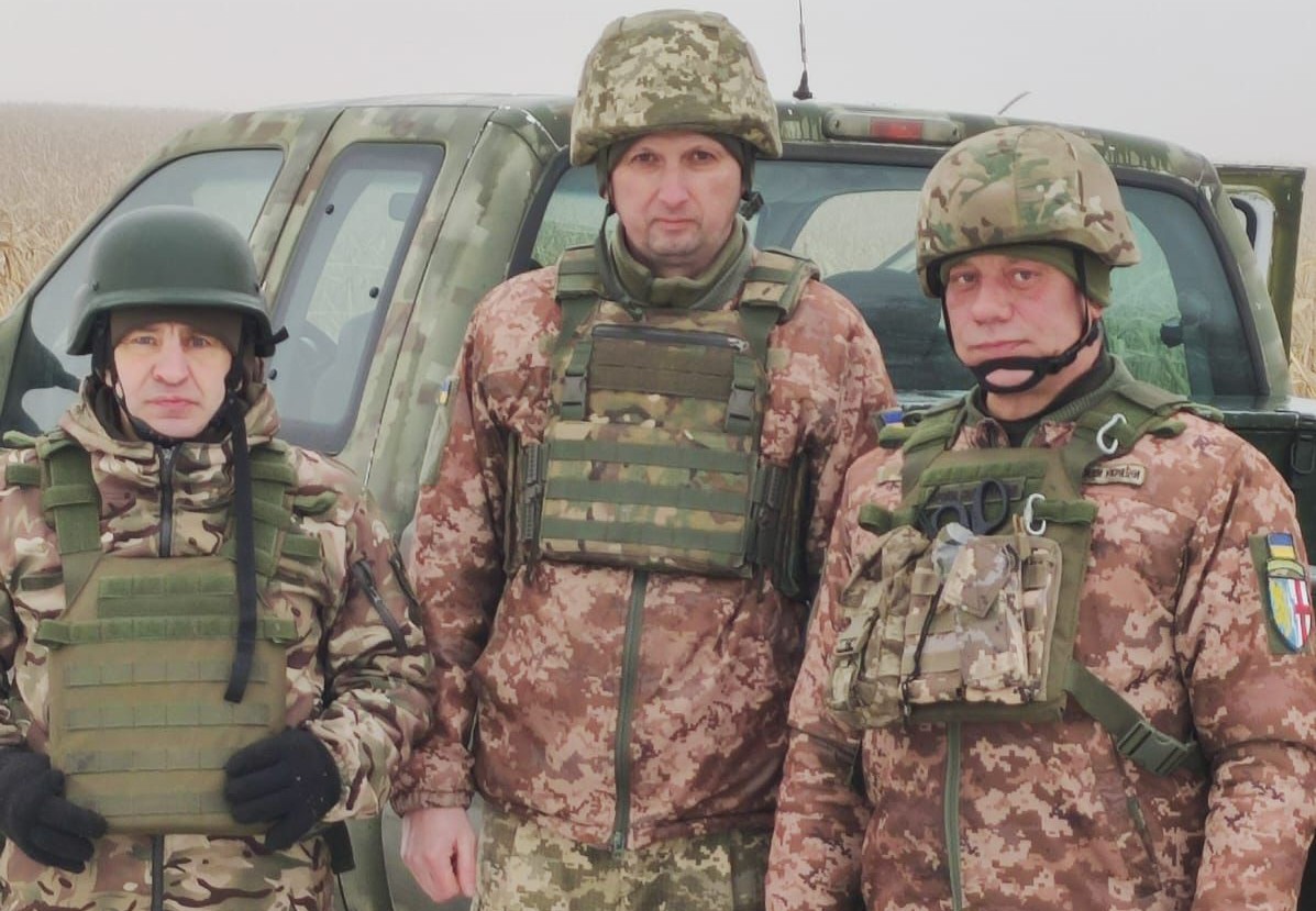 Воїни ЗСУ в бронежилетах і шоломах перед автомобілем.