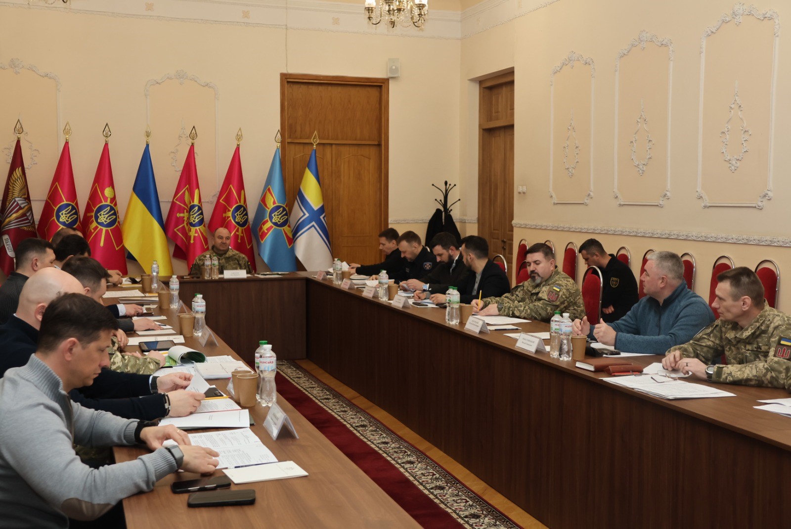 Нарада військового керівництва та фахівців за великим столом у залі, прикрашеній державним та відомчими прапорами України.