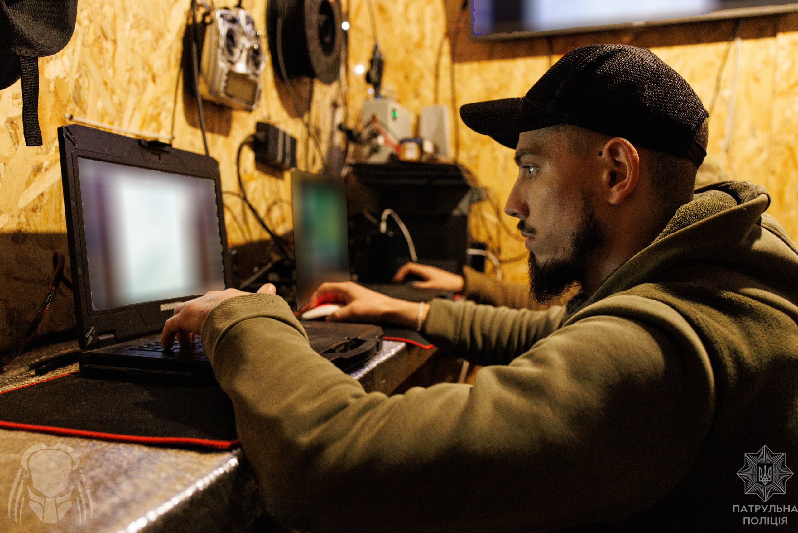 Оператор сидить у невеликому приміщенні та працює за ноутбуком, зосереджено дивлячись на екран. Навколо нього розміщене обладнання для керування або налаштування техніки.