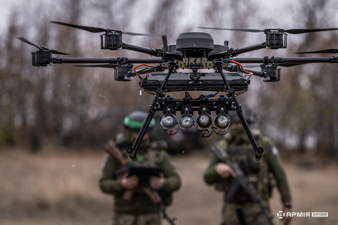 На передньому плані дрону типу "гексакоптер", на задбному плані силуети двох військових