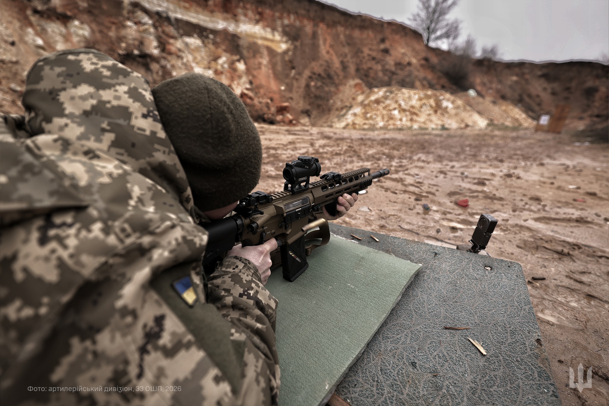 Український військовий веде стрільбу з автоматичної гвинтівки, займаючи позицію на стрілецькому рубежі. Боєць прицілюється у мішені на полігоні, використовуючи оптичний приціл.