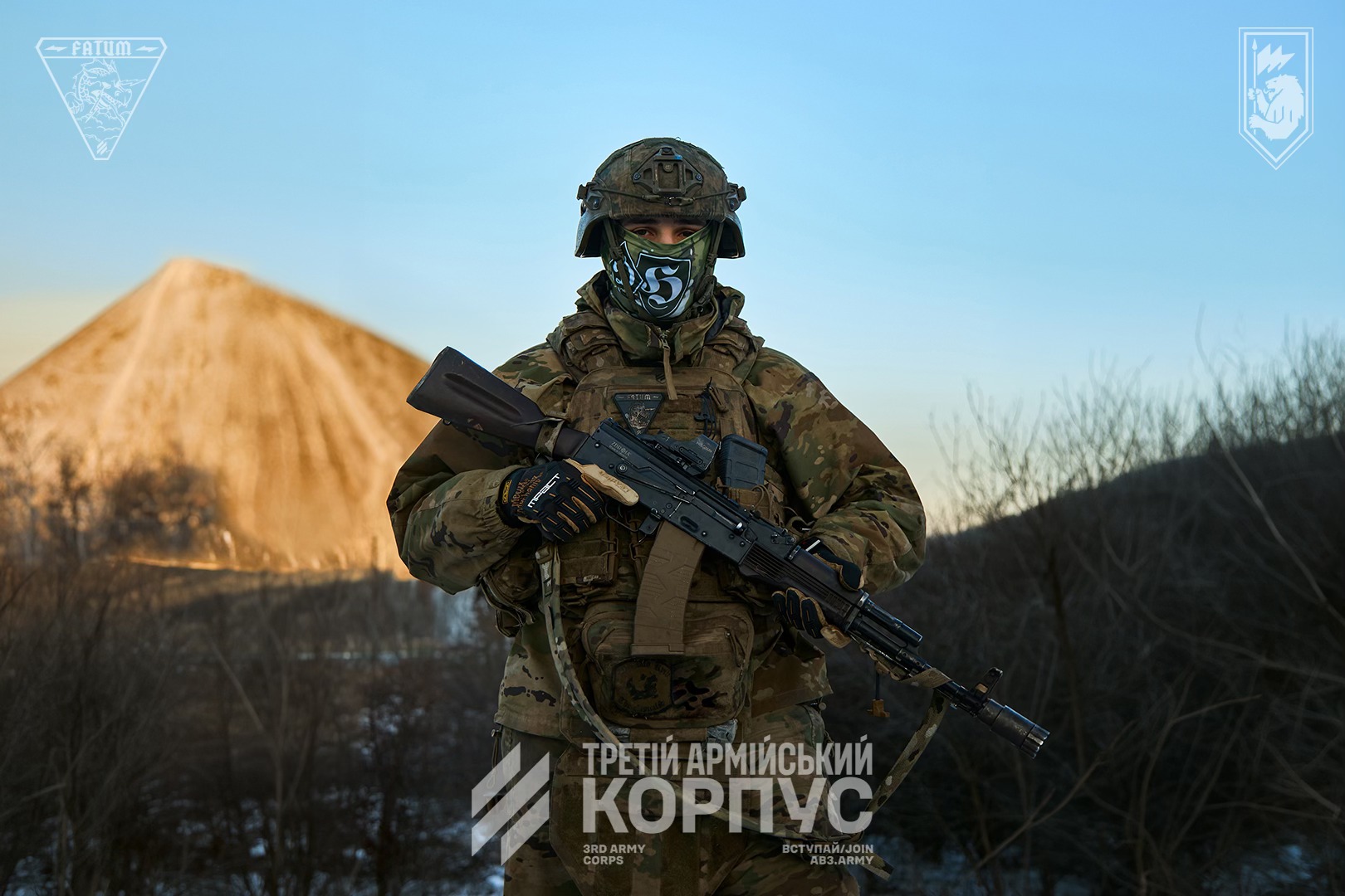 Військовий у камуфляжі та шоломі стоїть із автоматом у руках на тлі терикона, дивлячись прямо в камеру. На обличчі — маска, а внизу зображення розміщено напис «Третій армійський корпус».