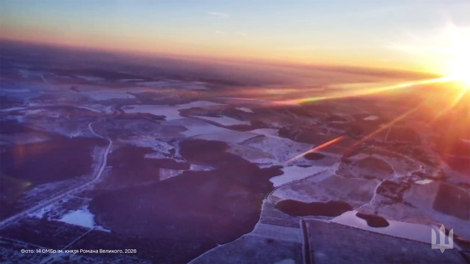З висоти пташиного польоту видно зимовий ландшафт із полями, лісосмугами та дорогами, частково вкритими снігом. Над горизонтом сходить сонце, його яскраві промені прорізають ранковий туман і освітлюють простір над лінією фронту.