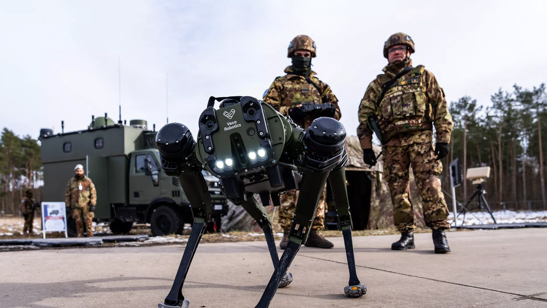 Робопес на передньому плані, за ним стоять двоє італійських військових