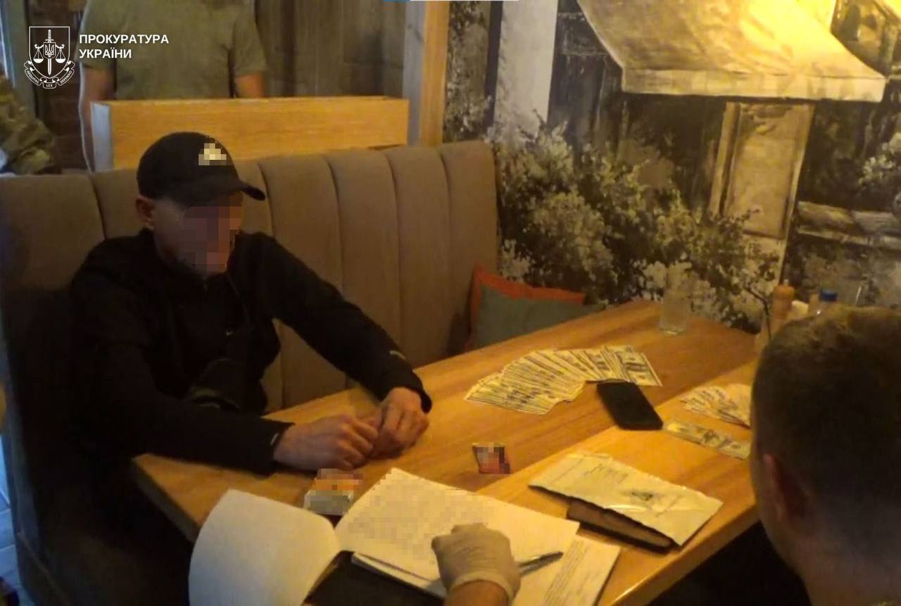 Двоє чоловіків сидять за столом на якому розкладені гроші та документи