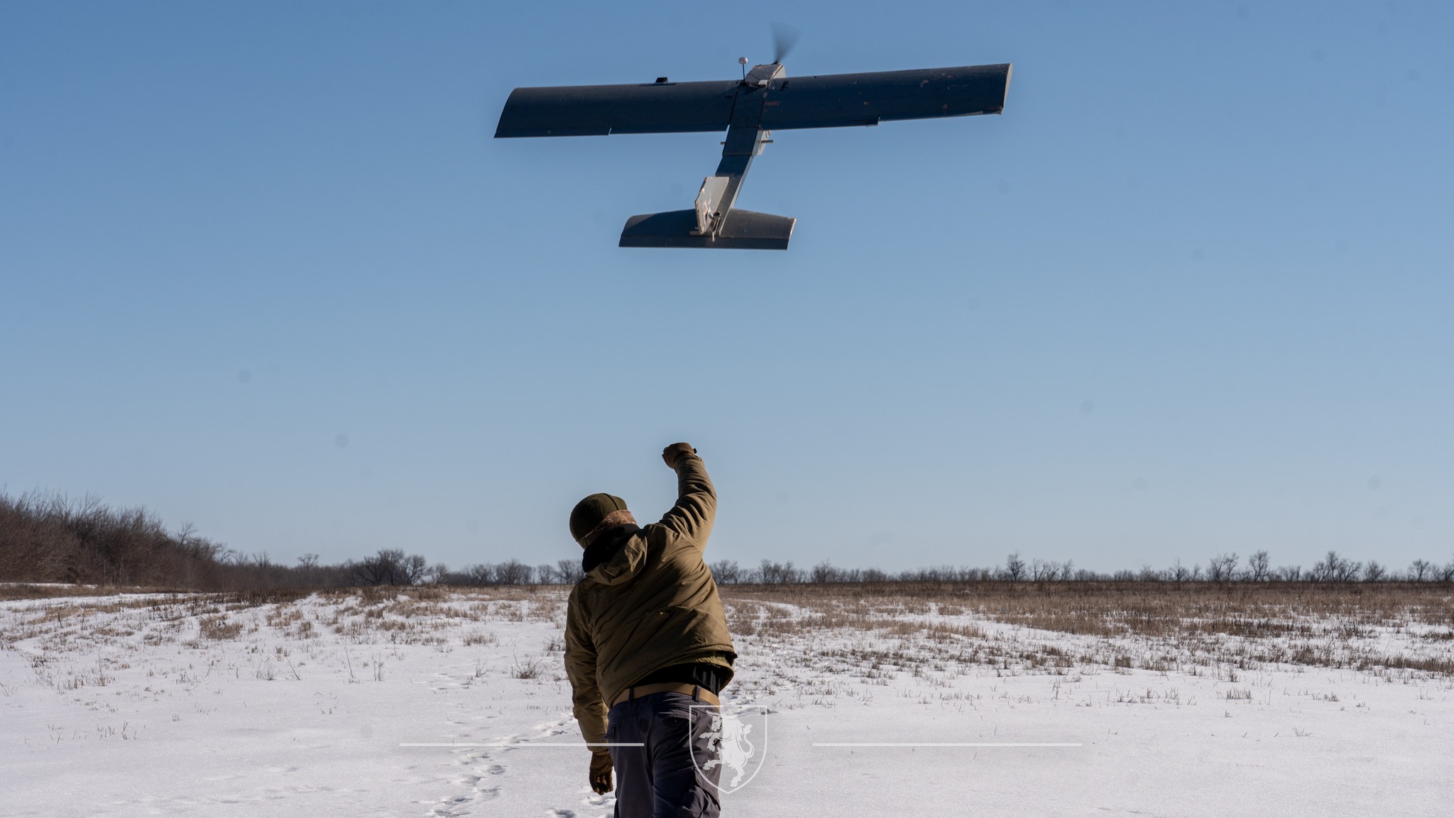 Боєць запускає безпілотник літакового типу, підкидаючи його в повітря на відкритій засніженій місцевості. Апарат уже набирає висоту, тоді як оператор стежить за його стартом.