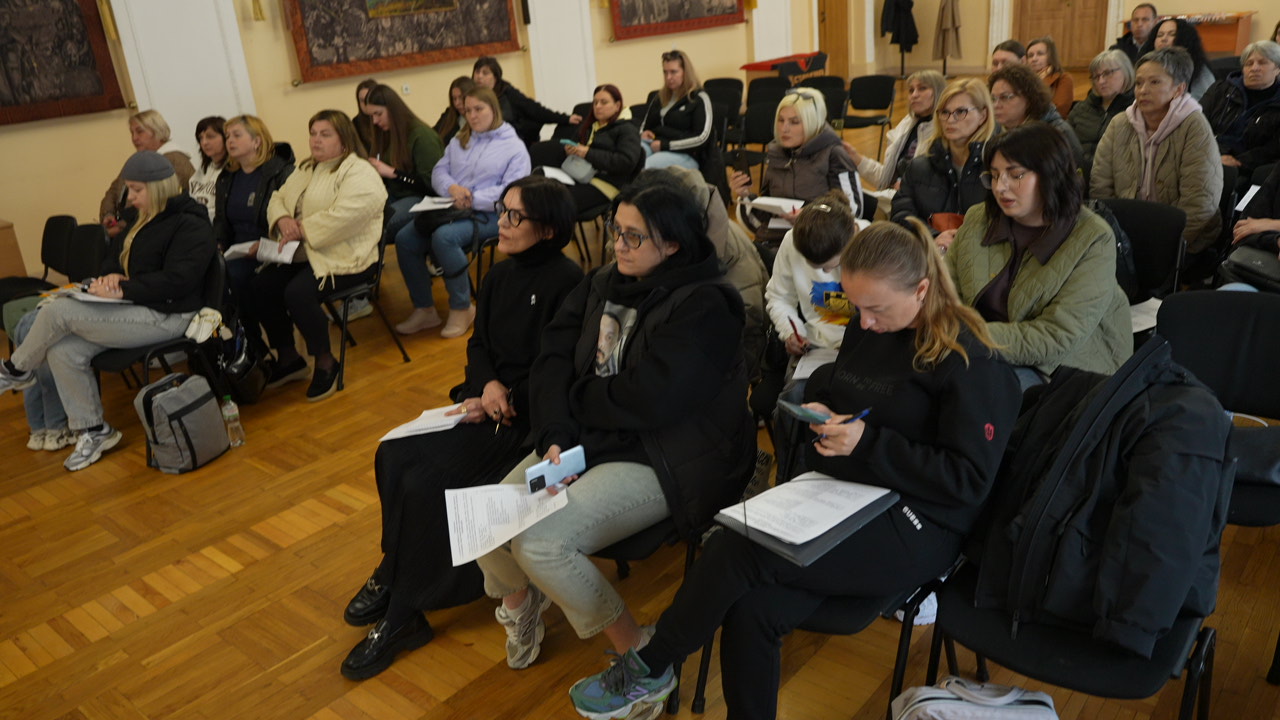 Учасники сидять рядами з документами в руках, дехто робить нотатки або перевіряє телефон. Видно, що це робоча зустріч із практичним обговоренням.