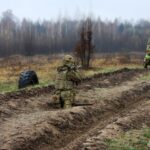 Боєць у траншеї прицілюється з гранатомета, готуючись до пострілу. Інший військовий поруч контролює обстановку та забезпечує прикриття.