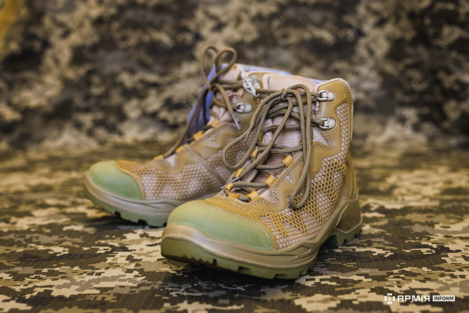 Пара тактичних черевиків світло-коричневого кольору стоїть на камуфляжній поверхні. Вони мають посилену підошву та сітчасті вставки для вентиляції.