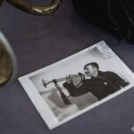 Поряд із сурмою лежить архівне фото музиканта, який тримає схожий духовий інструмент. Це підсилює історичний контекст експоната та демонструє його практичне використання.