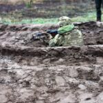 Військовий у траншеї веде вогонь із укриття, використовуючи земляний вал як захист. Рельєф місцевості свідчить про облаштовану систему окопів.