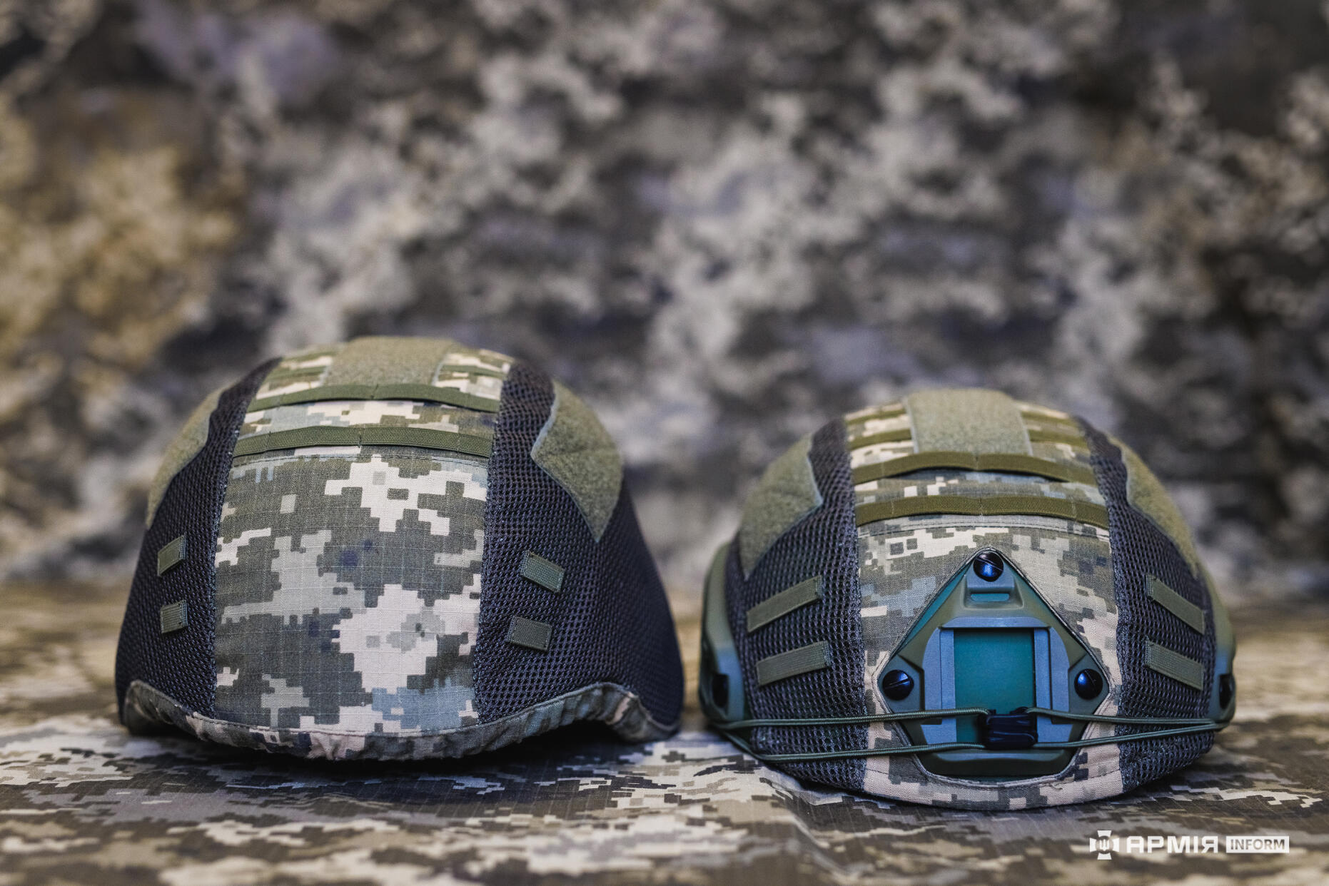 Два військові шоломи розміщені поруч, показуючи різні конструкції та елементи кріплення. Один оснащений переднім модулем для додаткового обладнання.