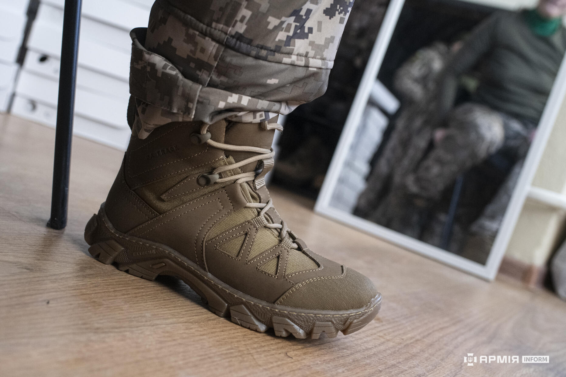 Черевик на нозі військового зображений у приміщенні, поруч видно відображення у дзеркалі. Добре помітна масивна підошва та надійна фіксація ноги для активного пересування.