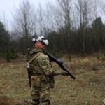 Військовий у VR-окулярах тримає тренувальну зброю, відпрацьовуючи дії в симульованому середовищі. Лісистий полігон створює реалістичні умови для навчання.