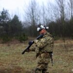 Військовий у VR-окулярах рухається полігоном, тримаючи тренувальну зброю на плечі. Навколо — лісиста місцевість, що створює умови, наближені до реальних.