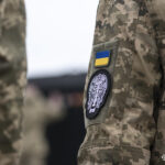Крупний план військової форми з нашивками — прапором України та емблемою підрозділу. Деталь підкреслює належність і символіку служби.