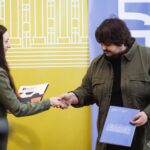 Під час церемонії відбувається вручення документів або відзнак між учасниками події. Фото фіксує момент офіційного нагородження чи партнерської співпраці.