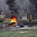 Військові просуваються повз вогонь і дим, діючи у складі підрозділу. Інструктор у світловідбивному жилеті контролює виконання вправи.