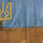 Крупний план історичного синьо-жовтого прапора демонструє вишитий тризуб та збережені кольори полотна. Артефакт символізує українську державність і військову традицію.