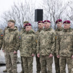 Група військовослужбовців у камуфляжі стоїть у строю, більшість із них у бордових беретах. Їхні обличчя зосереджені, а постава підкреслює дисципліну й урочистість моменту.