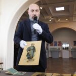 Чоловік-експерт під час презентації демонструє один із історичних ілюстративних матеріалів виставки. Його виступ поєднує науковий коментар із показом архівних експонатів.