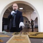 На фото спікер проводить екскурсію експозицією, пояснюючи відвідувачам значення представлених артефактів. Перед ним розміщені прапори, документи та художні матеріали доби УНР.