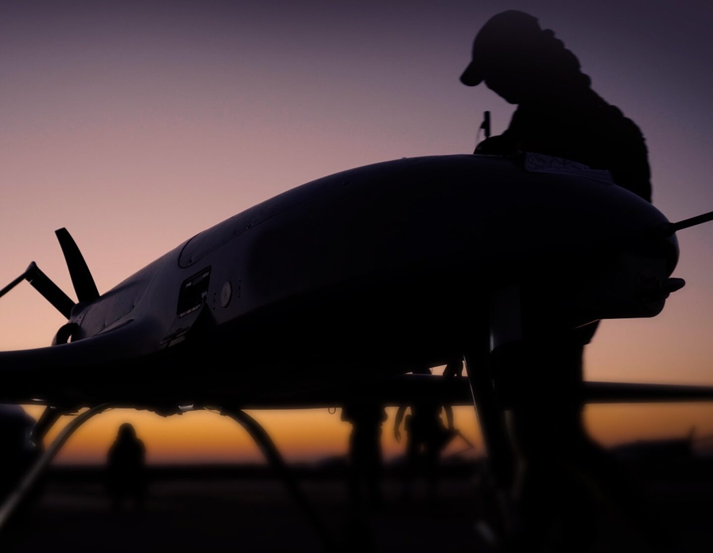 На фото — силует військового поруч із безпілотником на тлі заходу сонця, що створює контраст між темною фігурою і теплим небом. Унизу видно логотипи підрозділу, а загальна композиція підкреслює зосередженість і технологічний характер роботи.