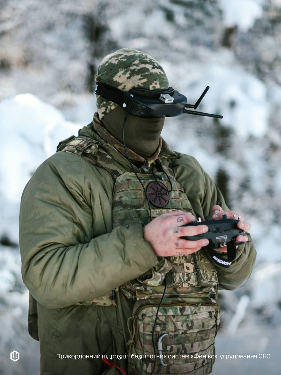 Військовослужбовець прикордонного підрозділу безпілотних систем у зимових умовах керує дроном, використовуючи FPV-окуляри та пульт дистанційного управління. Фото акцентує увагу на сучасному оснащенні оператора, його екіпіруванні та технологічному характері бойових завдань.