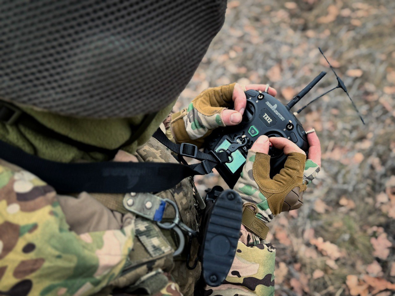 Військовослужбовець у захисному спорядженні керує пультом дистанційного управління, зосереджено контролюючи роботу безпілотної системи або наземного роботизованого комплексу. Крупний ракурс підкреслює точність дій оператора, деталі екіпірування та технологічний характер сучасної бойової роботи.