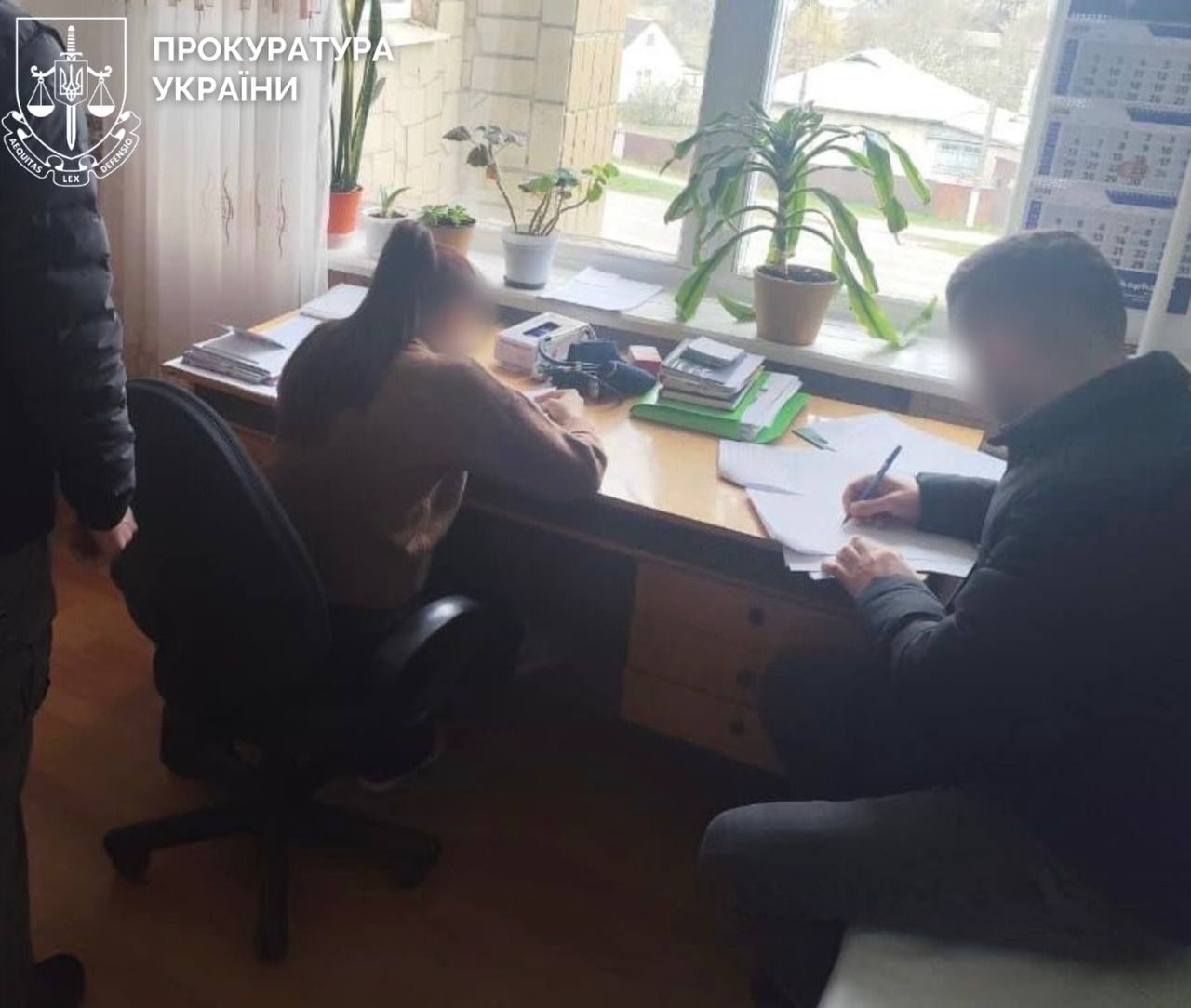 Жінка сидить за столом, поруч правоохоронець