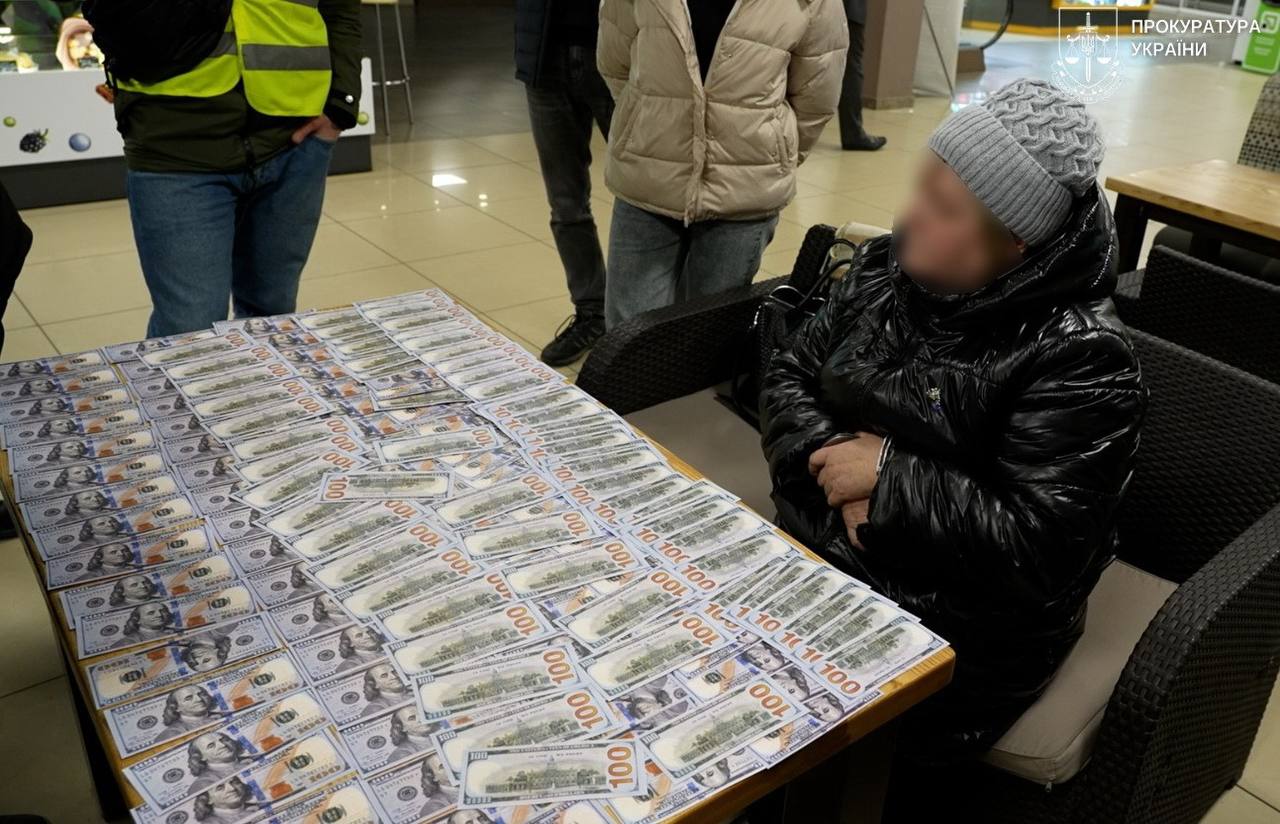 Жінка сидить за столом на якому лежать доларові купюри