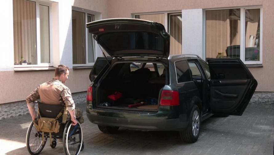 Ветеран у кріслі колісному поруч з легковим автомобілем