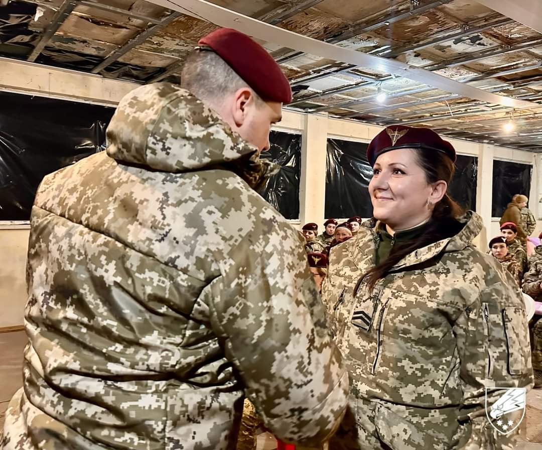 Військова у зимовому польовому однострої та бордовому береті бере участь у церемонії чи службовому заході серед побратимів. Атмосфера кадру передає повагу, дисципліну та згуртованість десантного підрозділу.