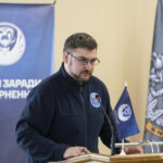 Представник організації виступає за трибуною перед делегатами та учасниками конференції. Банер «Разом заради повернення» акцентує на головній тематиці заходу.