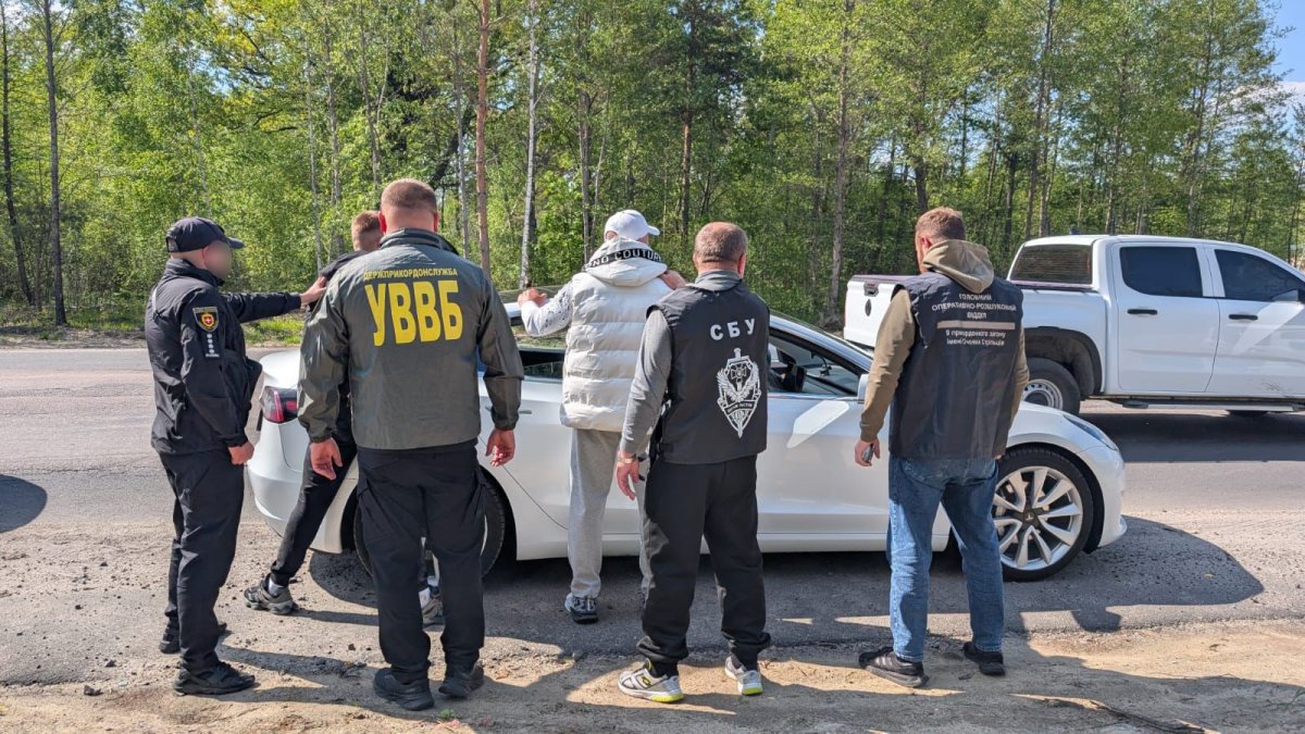 Затримані стоять обличчям до свого авто. Їх охороняють правоохоронці