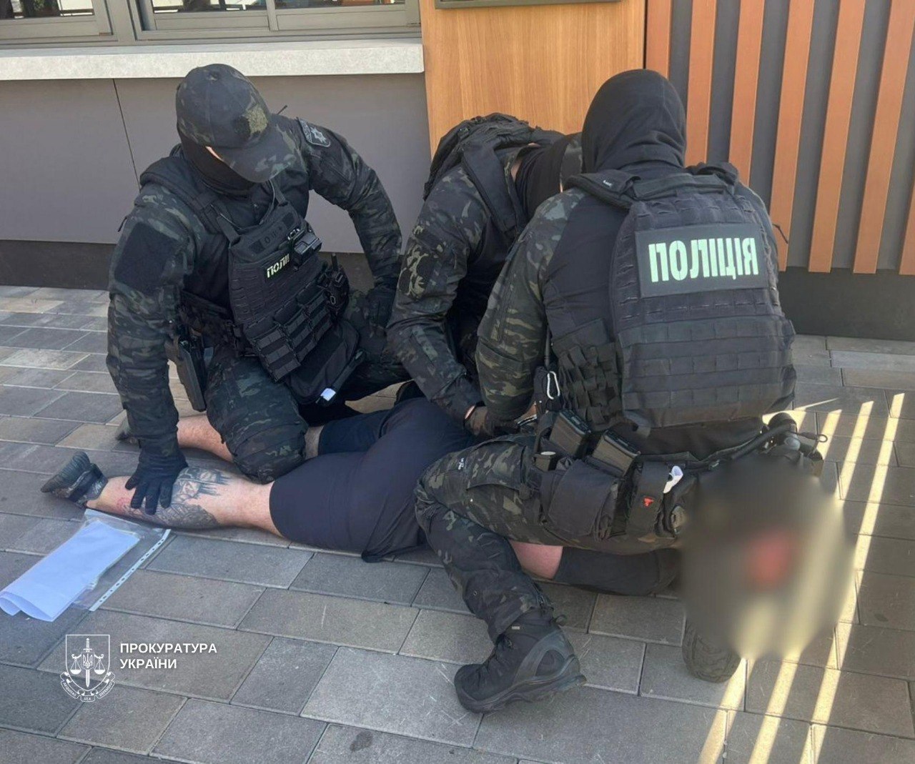 Затриманий оежить на підлозі, над ним сидять правоохоронці