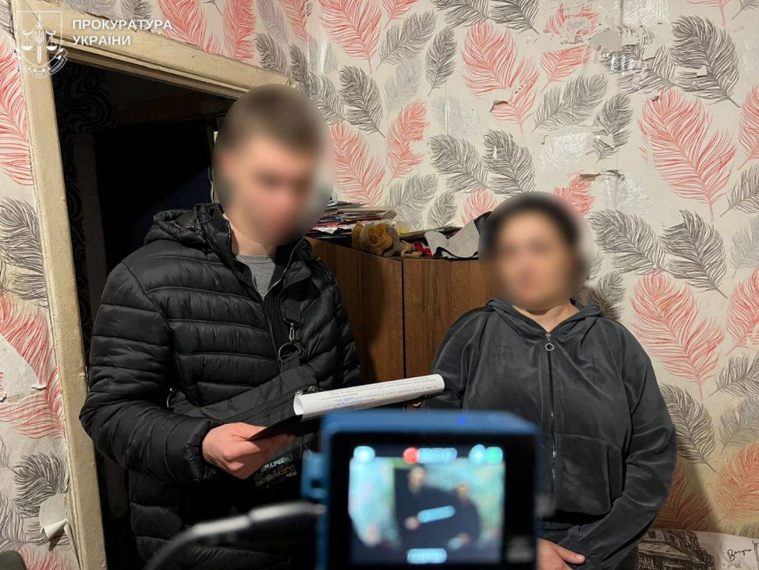 Затримана стоїть у кімнаті. Поруч правоохоронець