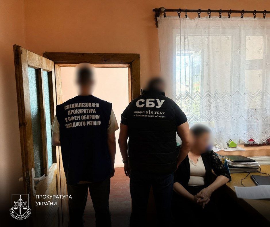 Жінка сидить за столом, поруч стоять правоохоронці