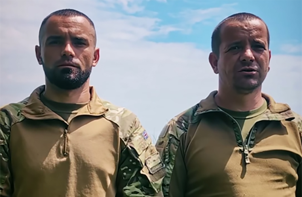 Двоє чоловіків у військовій формі стоять поруч просто неба на тлі блакитного неба. Обидва мають зосереджений і серйозний вигляд, що надає кадру стриманого та напруженого настрою
