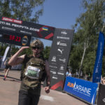Військовий у спорядженні проходить під фінішною аркою та підносить руку до шолома. Його жест виглядає як вітання або знак пошани після завершення дистанції.