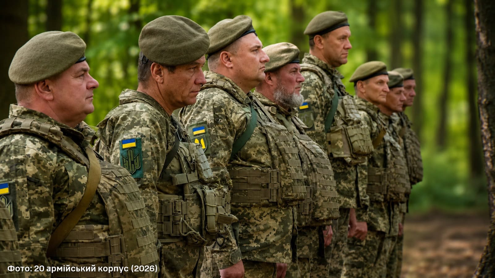 Військовослужбовці 20 армійського корпусу в камуфляжній формі та беретах вишикувалися у лісі. На одностроях видно українські прапори й шеврони, а самі військові зосереджено дивляться вперед.