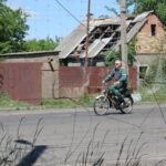 Місцевий житель прифронтового населеного пункту їде на велосипеді по дорозі, вкритій протидроновою сіткою